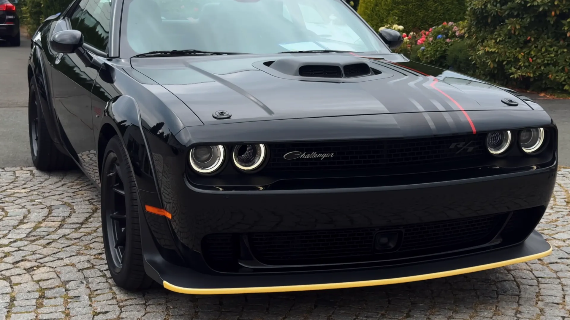 Чёрный Dodge Challenger 2023 с жёлтой полосой на переднем спойлере стоит на брусчатке